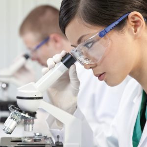 Chinese Female Woman Scientist & Microscope In Laboratory A Chinese Asian female medical or scientific researcher or doctor using a microscope in a laboratory with her colleague out of focus behind her.
